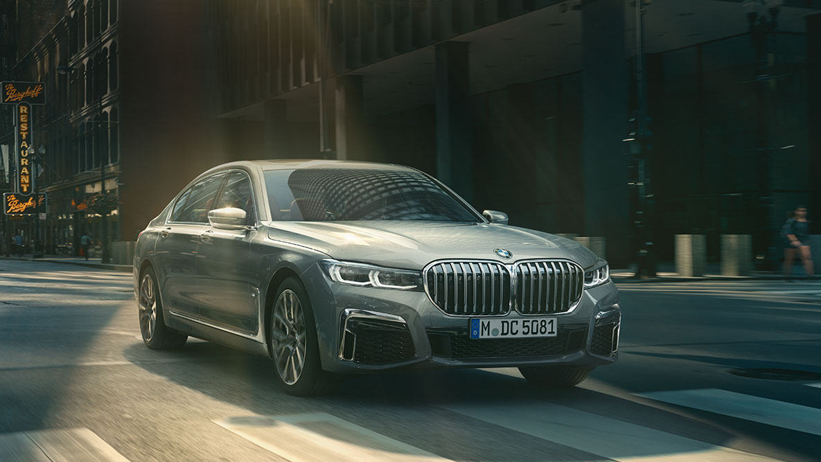 Driving Assistant Professional: three-quarter front view of BMW 7 Series Sedan driving in front of urban setting BMW 7 Series Sedan Driving Assistant Professional